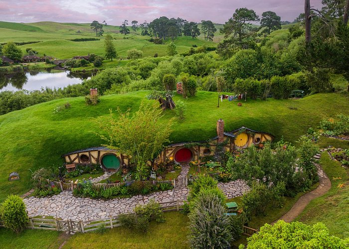 Scenic view of the Hobbiton Movie Set in New Zealand, featuring charming hobbit hole homes built into lush green hills, colorful round doors, and a picturesque countryside landscape. A must-visit destination for Lord of the Rings fans and luxury travelers seeking unique experiences