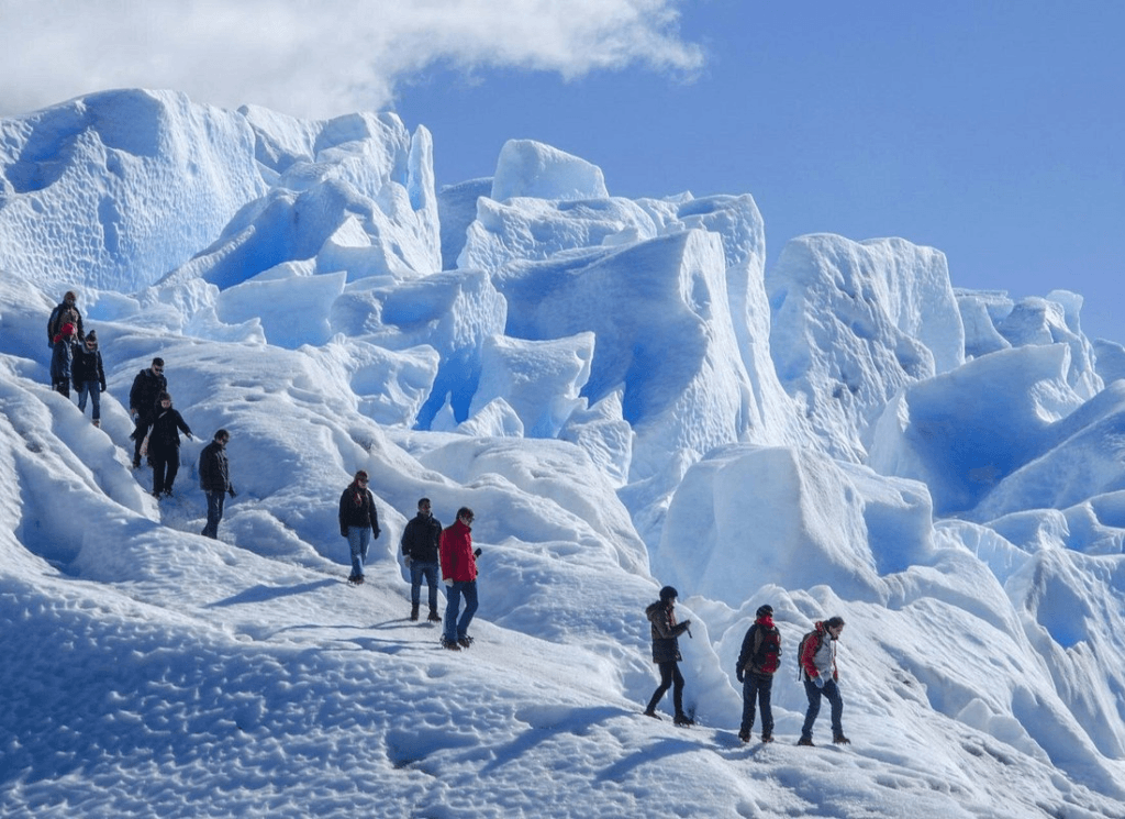 Luxury hikers traverse the stunning icy landscape of Patagonia, surrounded by towering blue glaciers under a clear sky, experiencing an exclusive high-end adventure